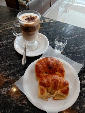 Café y pasteles sobre una barra de mármol negro. También hay un vaso de agua.