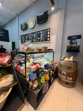 Un mostrador de delicatessen con diversos bocadillos y alimentos, un barril de madera y un tablero de menú.