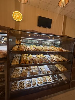 Vitrina de panadería llena de diversos pasteles y productos horneados bajo luces brillantes.