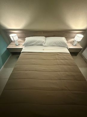 Dormitorio con cama, almohadas, edredón marrón, mesitas de noche, lámparas y paredes neutrales.