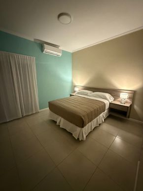 Dormitorio con cama, mesitas de noche y aire acondicionado. Paredes en tonos verde azulado y beige.