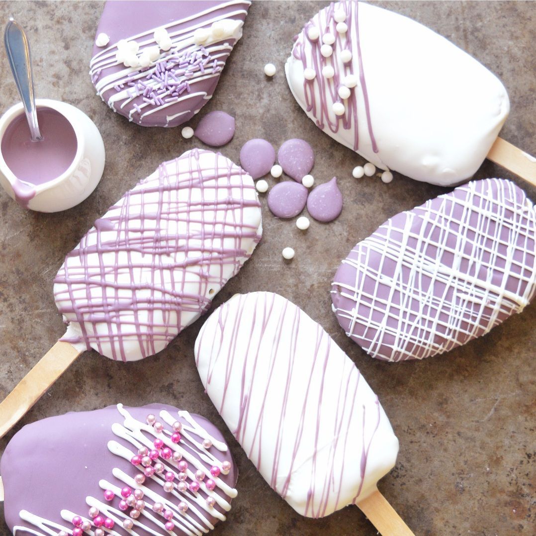 Diverse paarse en witte cakepops op stokjes, geglazuurd met glazuur, besprenkeld met witte chocolade, met hagelslag en dipsaus.
