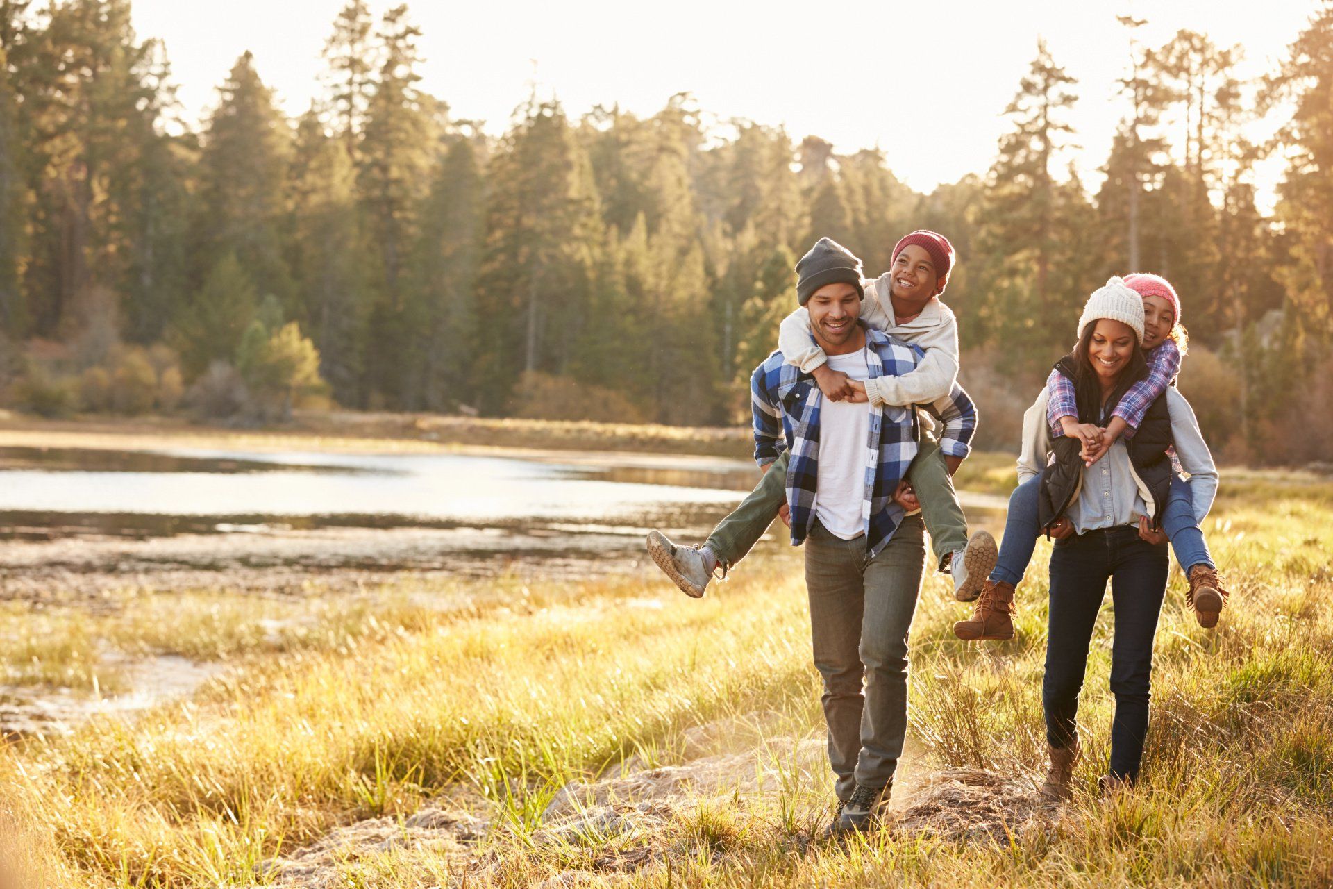 A family is walking in a field with a man carrying two children on his shoulders.