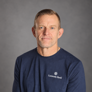 Portrait of a man in a navy Luminary Bank shirt against a gray background