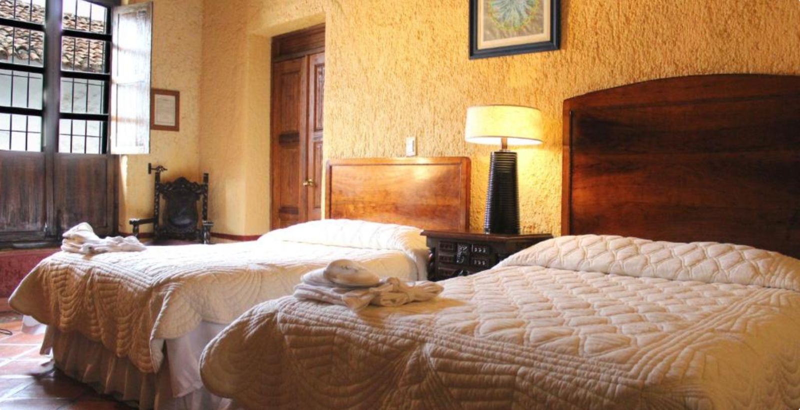 Habitación de hotel con dos camas sin hacer, una lámpara encendida y cálidas paredes revestidas de madera