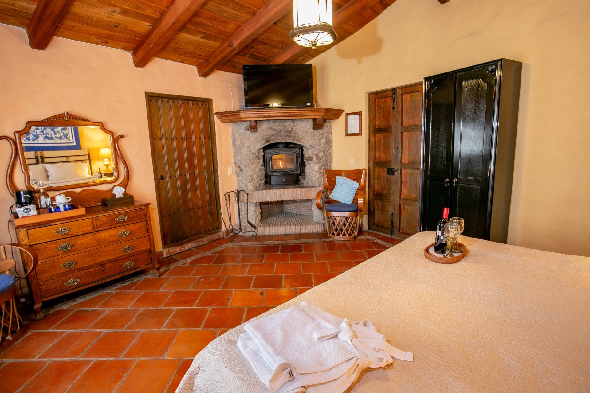 Bedroom with bed, orange accents, chairs, dark wooden beams and door.