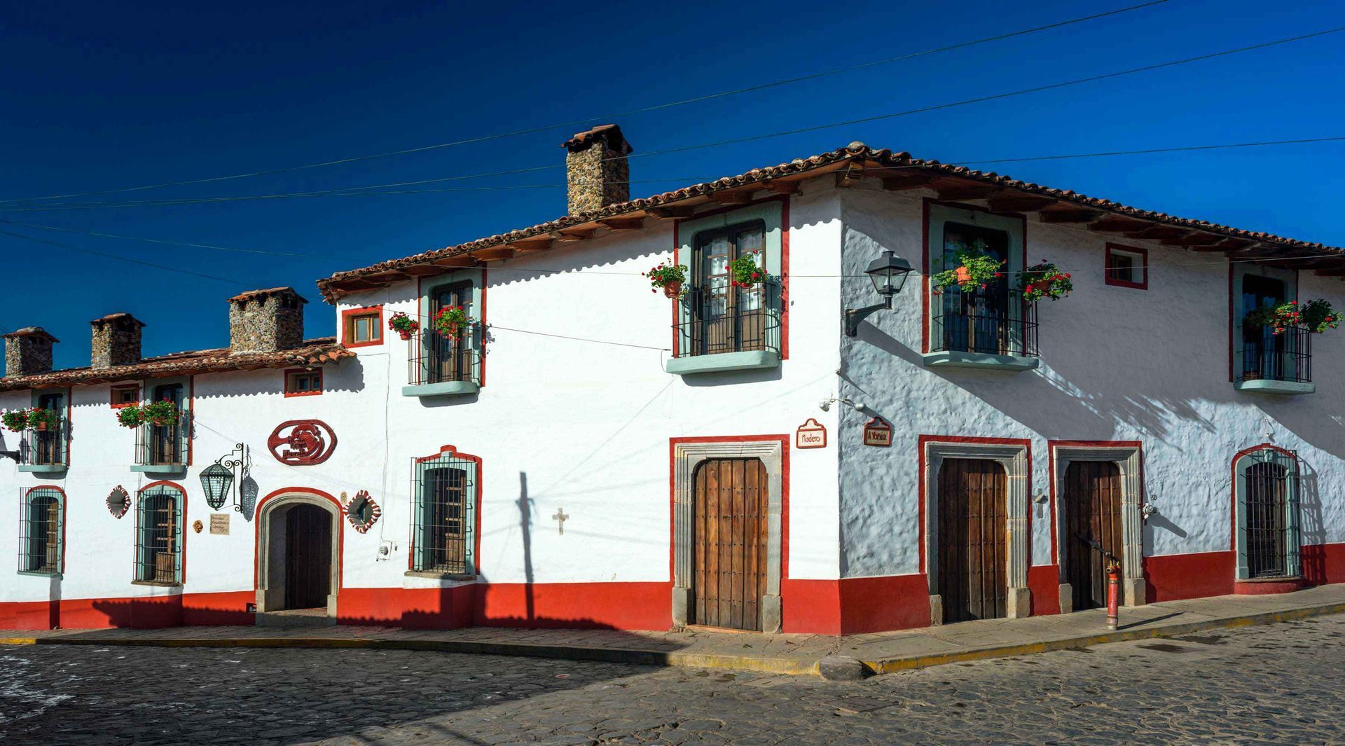 Edificio blanco de estuco con molduras rojas y puertas de madera en una calle soleada, visto desde la esquina