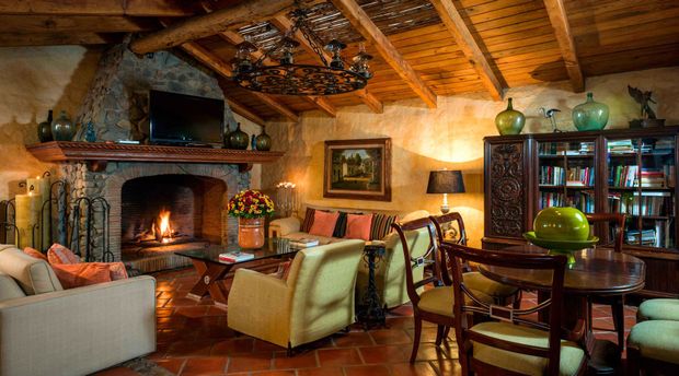 Acogedora sala de estar de estilo rústico, con chimenea de piedra, iluminación cálida, sofá rojo, sillones y mesa de comedor