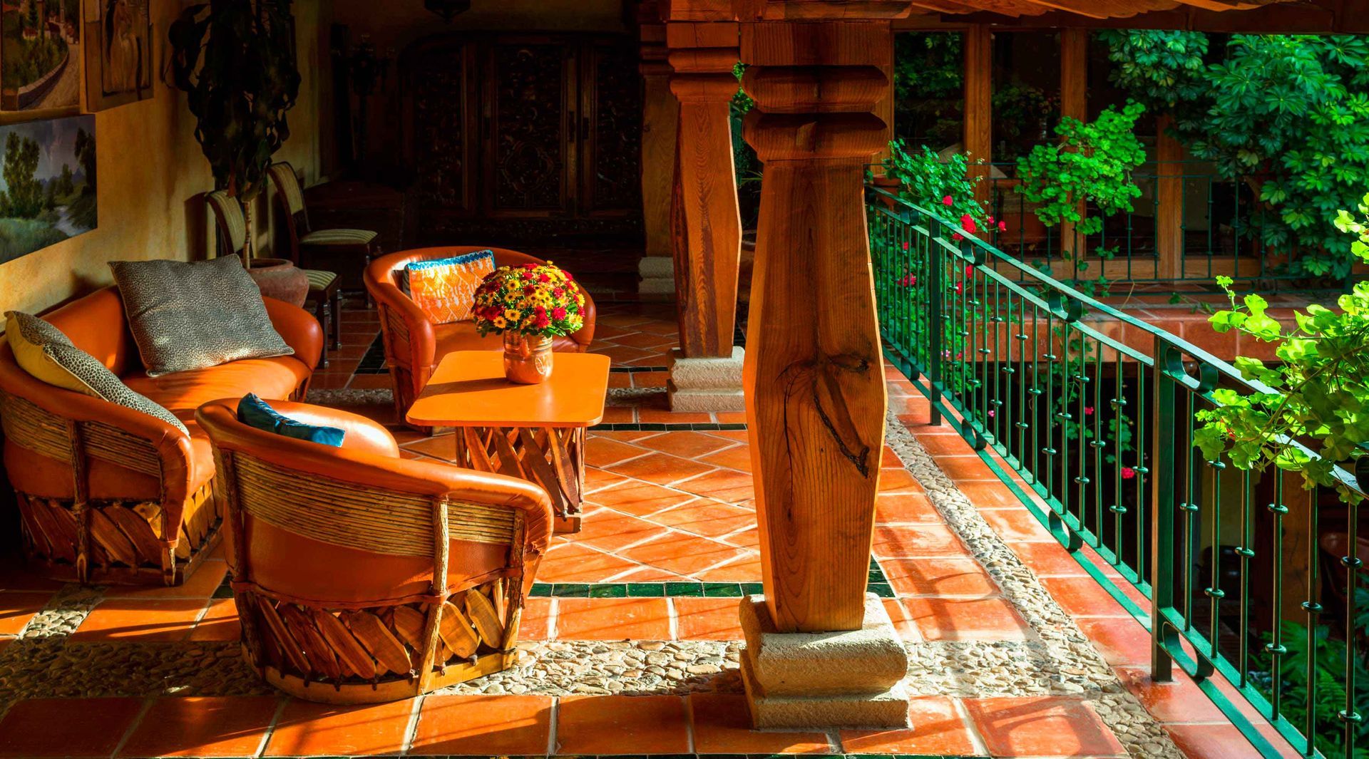 Patio soleado con sillas de mimbre, suelo de terracota y una barandilla verde con vistas a una exuberante vegetación