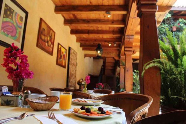 Acogedora mesa de desayuno en el patio, con fruta, zumo y flores bajo una pérgola de madera