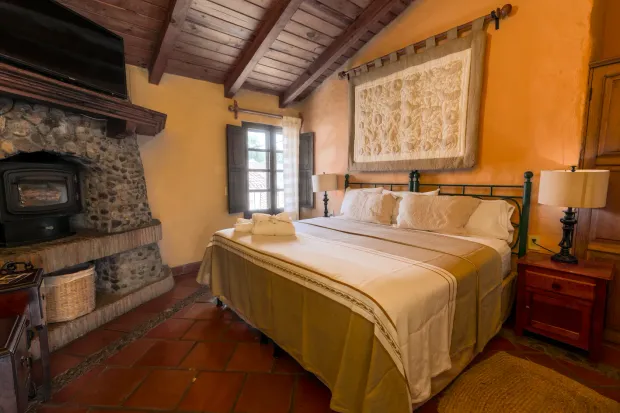 Acogedor dormitorio rústico con chimenea de piedra, vigas de madera y una cama bien hecha junto a la ventana.