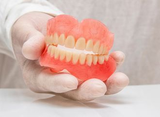 Hand holding dental model showing a denture attached to two implants. Pink gums, white teeth.