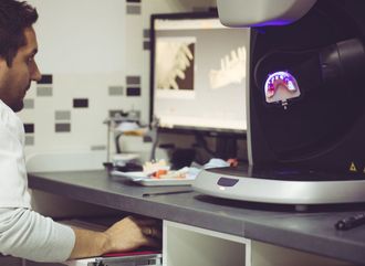 Man using a dental scanner, looking at a computer screen showing dental imagery.