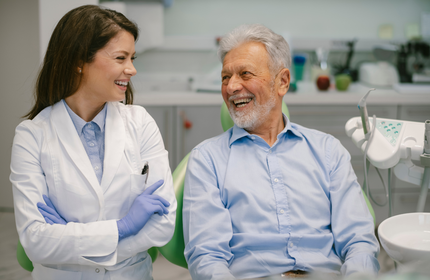 Dentist and patient smiling together in a dental office. Dentist in lab coat, patient in blue shirt.