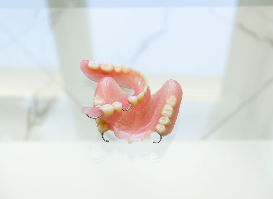 A partial dental prosthesis, pink with white teeth and metal clasps, sits on a reflective surface.