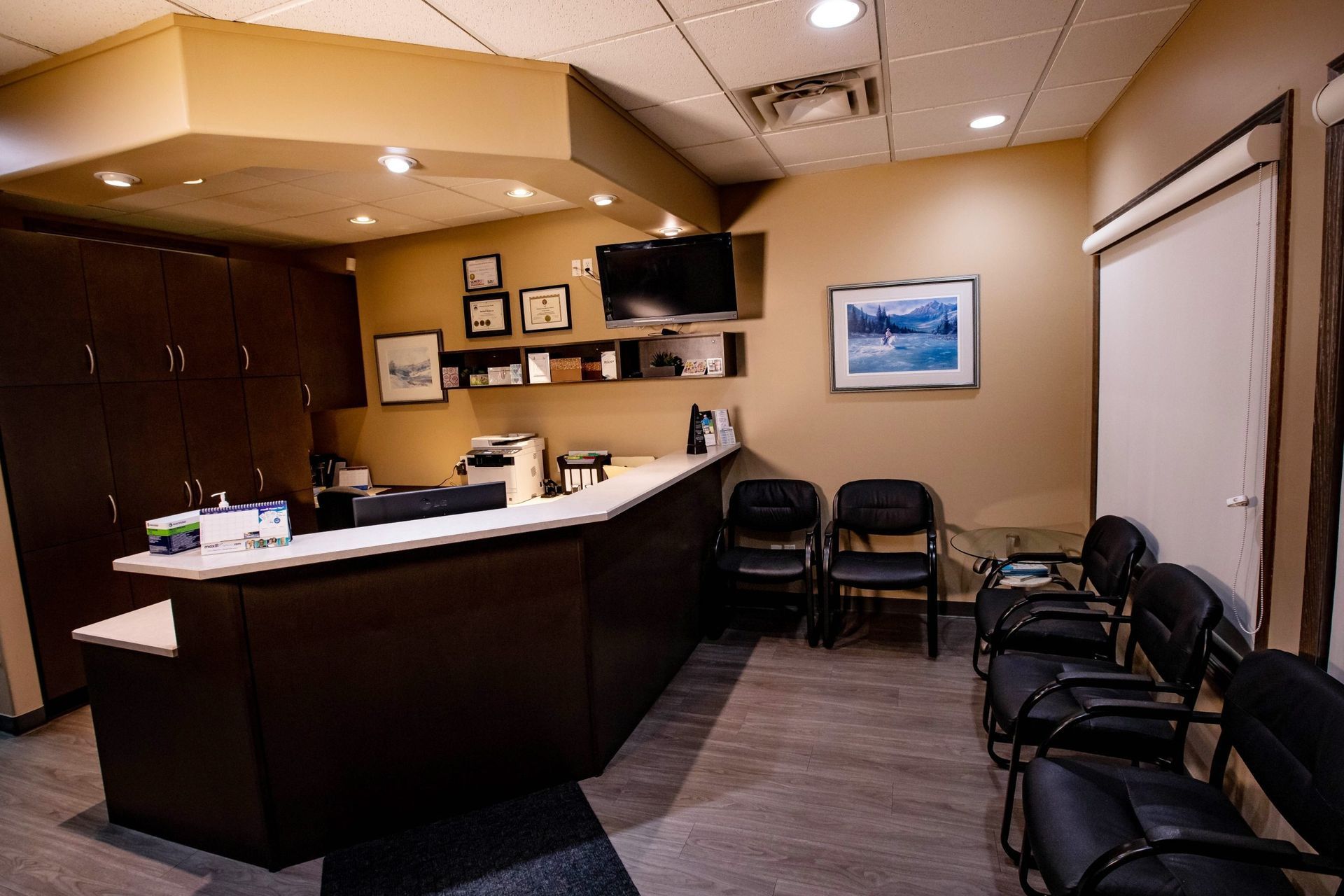 Reception area with a dark brown desk, waiting chairs, and wall-mounted TV.