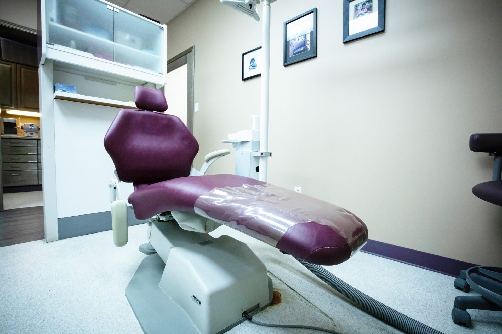 Dental chair in a light-colored room with cabinets, framed pictures, and dental equipment.