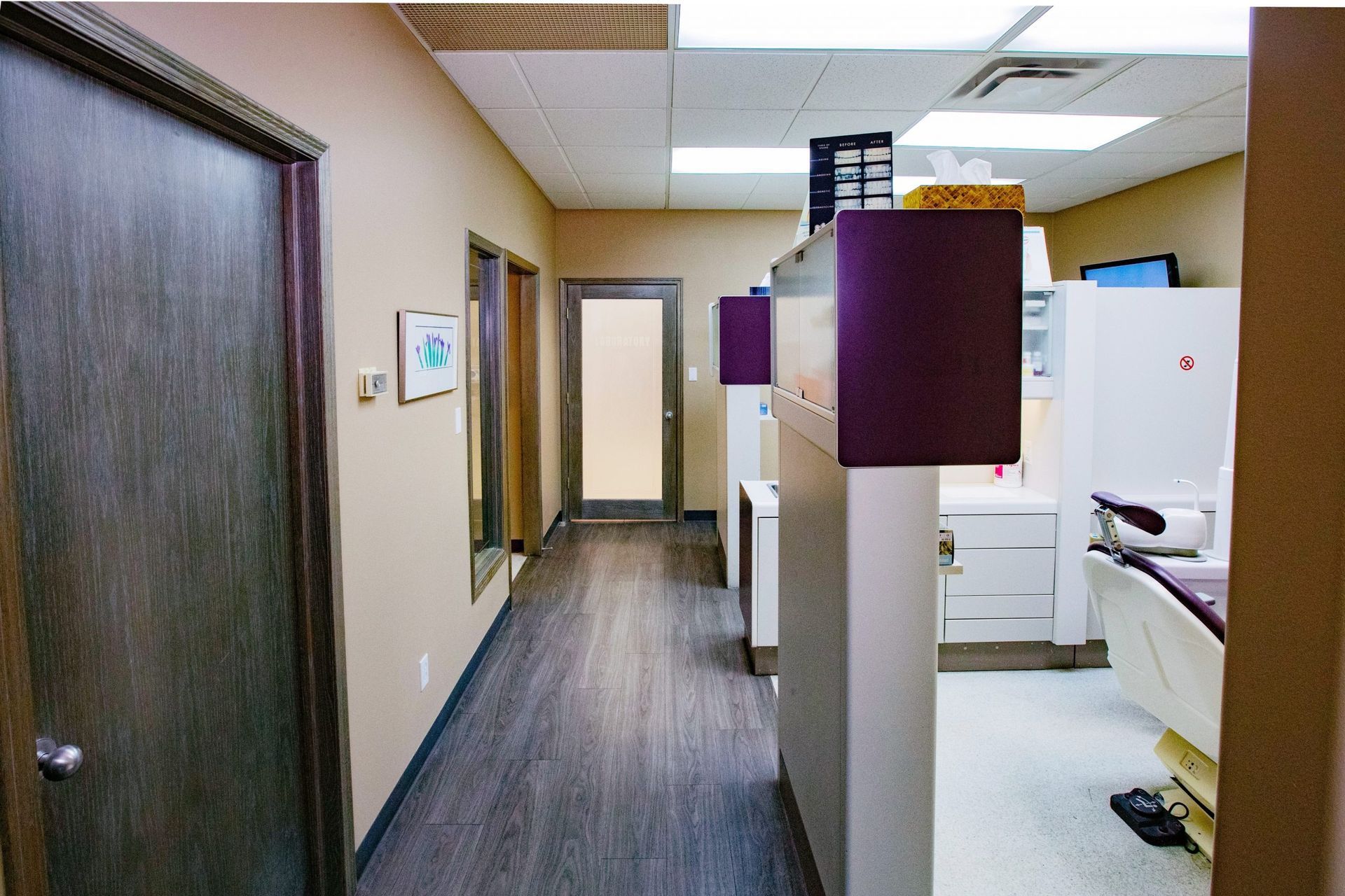Hallway in a dental office with patient rooms, neutral walls, dark wood doors and flooring.