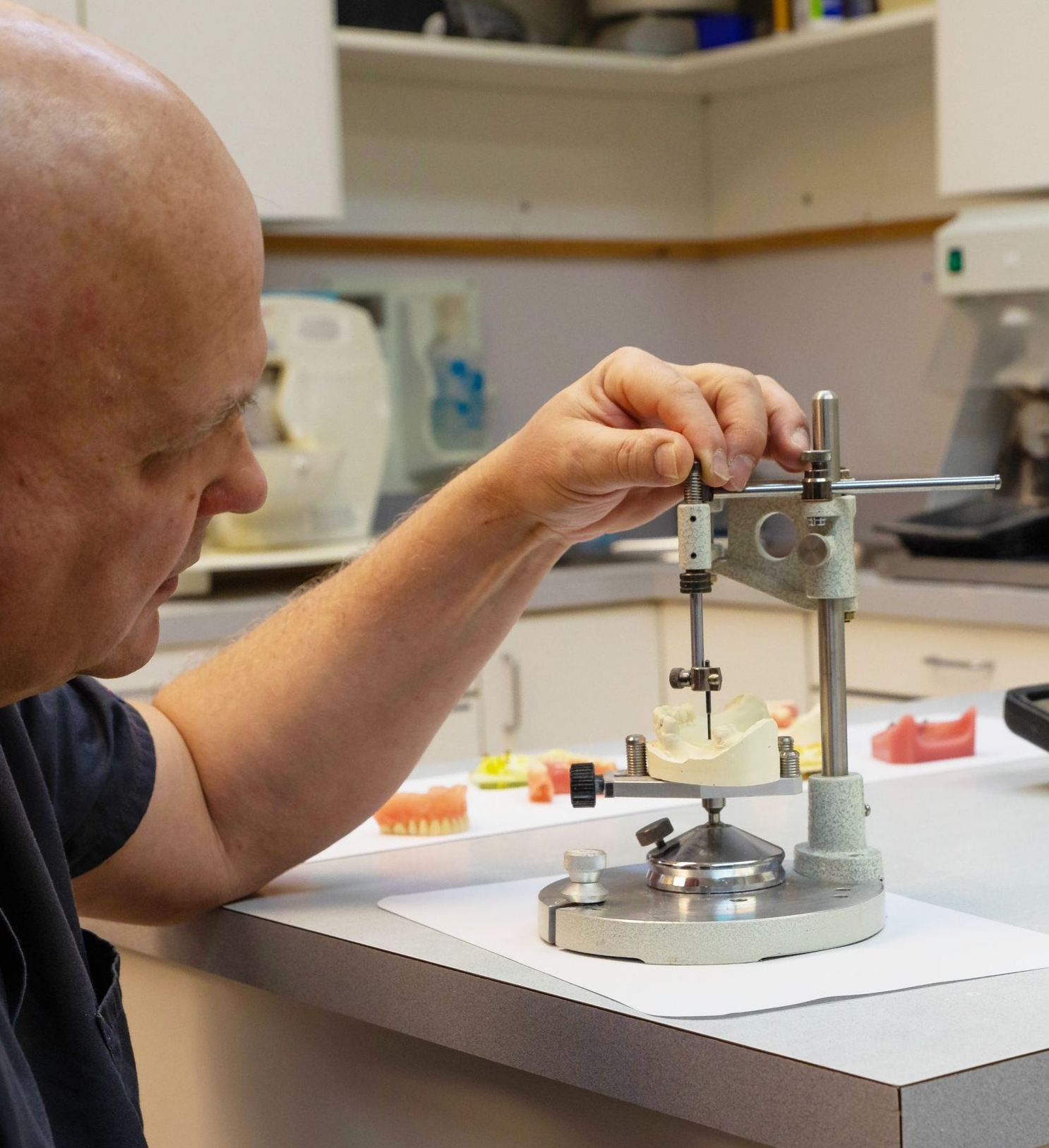 Man working on dental molds with an articulator in a dental lab.