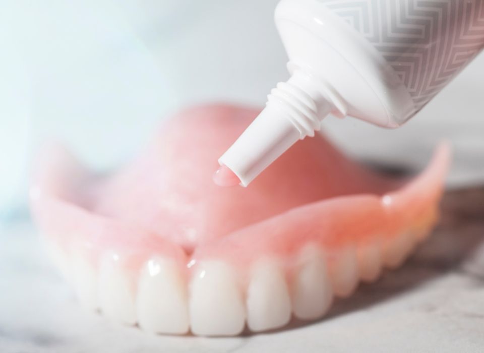 A tube dispensing adhesive onto a set of dentures.