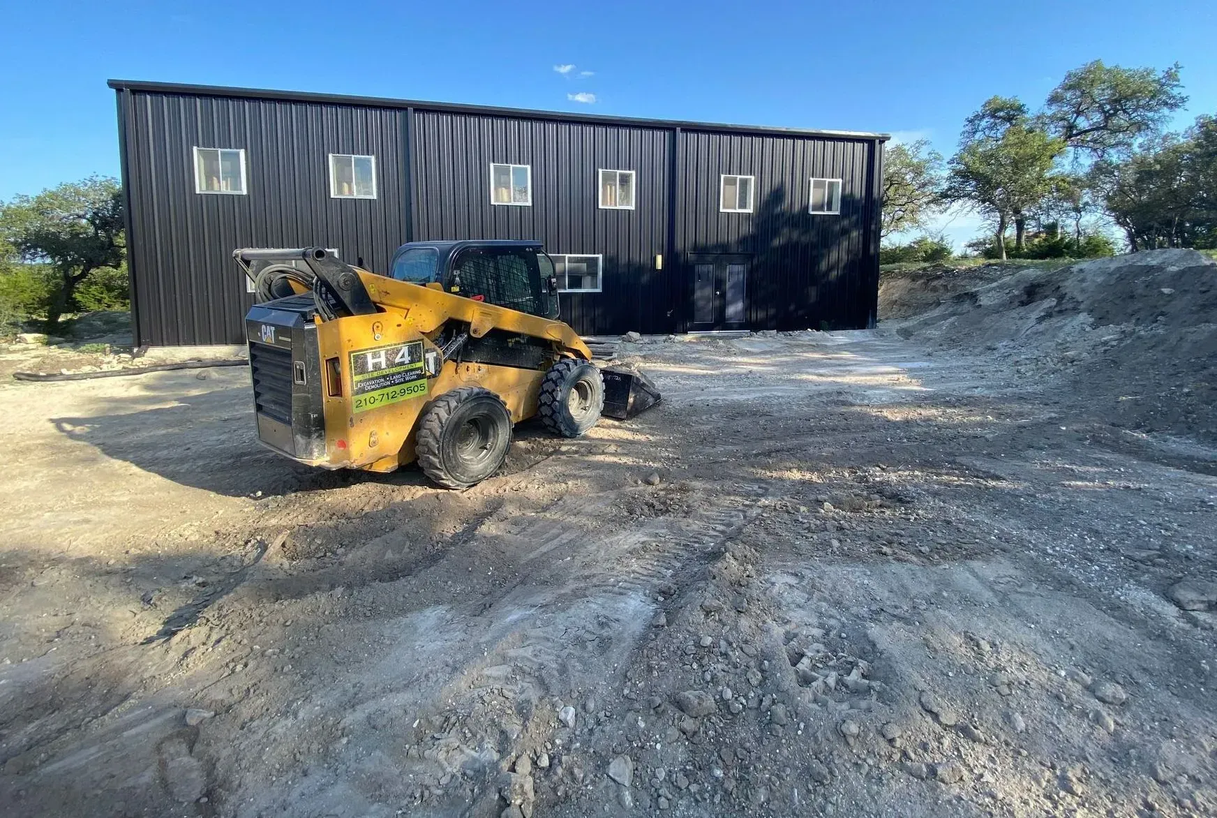 Yellow skid steer parked in front of a dark building on a gravel lot.