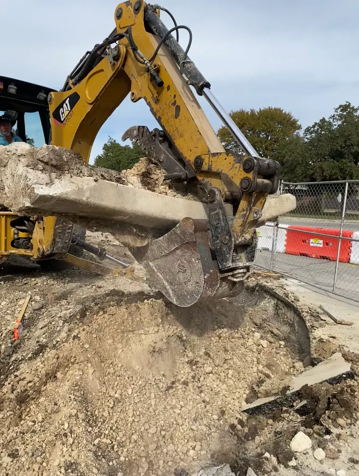 Yellow excavator lifting concrete slab from a construction site.