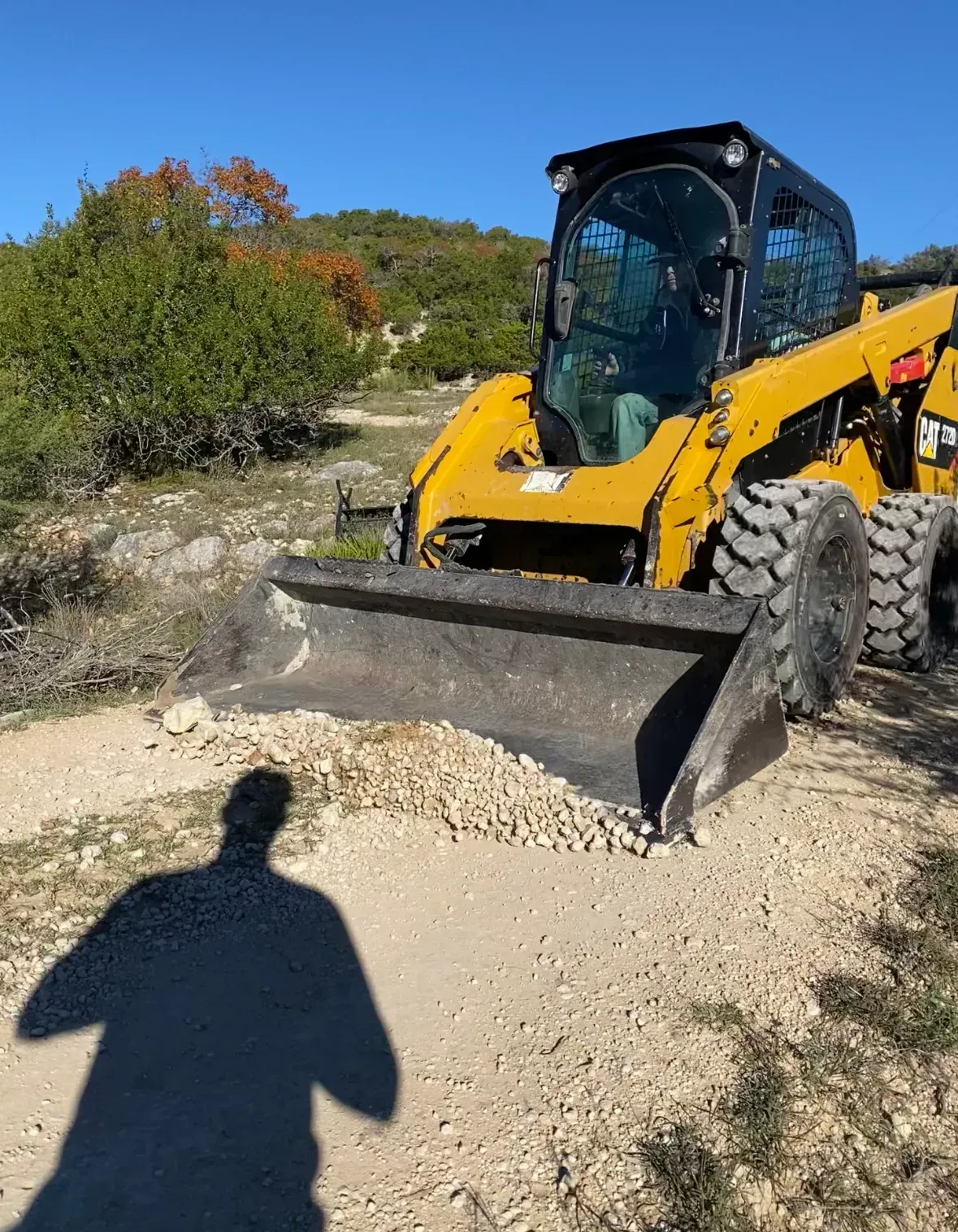 Yellow skid steer grading a gravel road on a sunny day.
