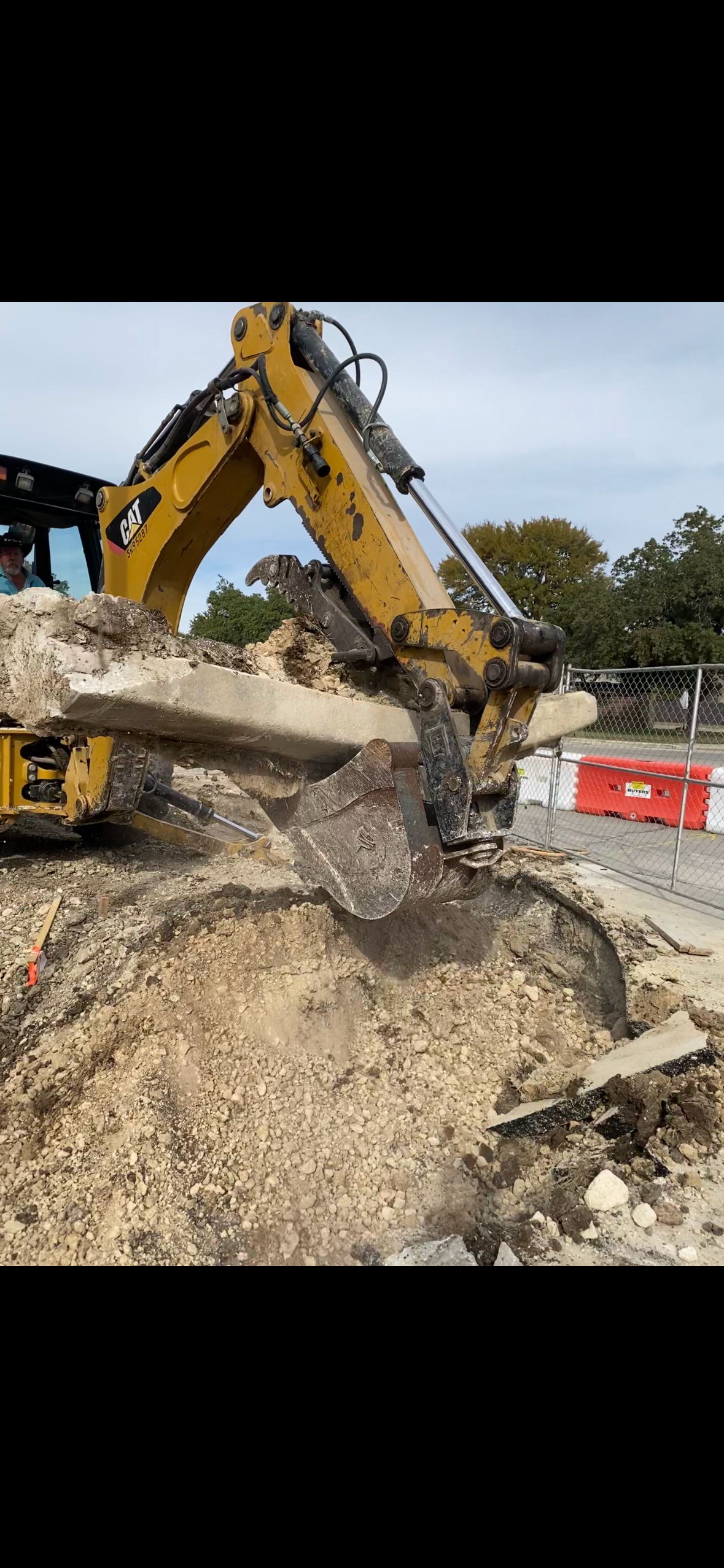 Excavator bucket digging a narrow trench in brown soil.