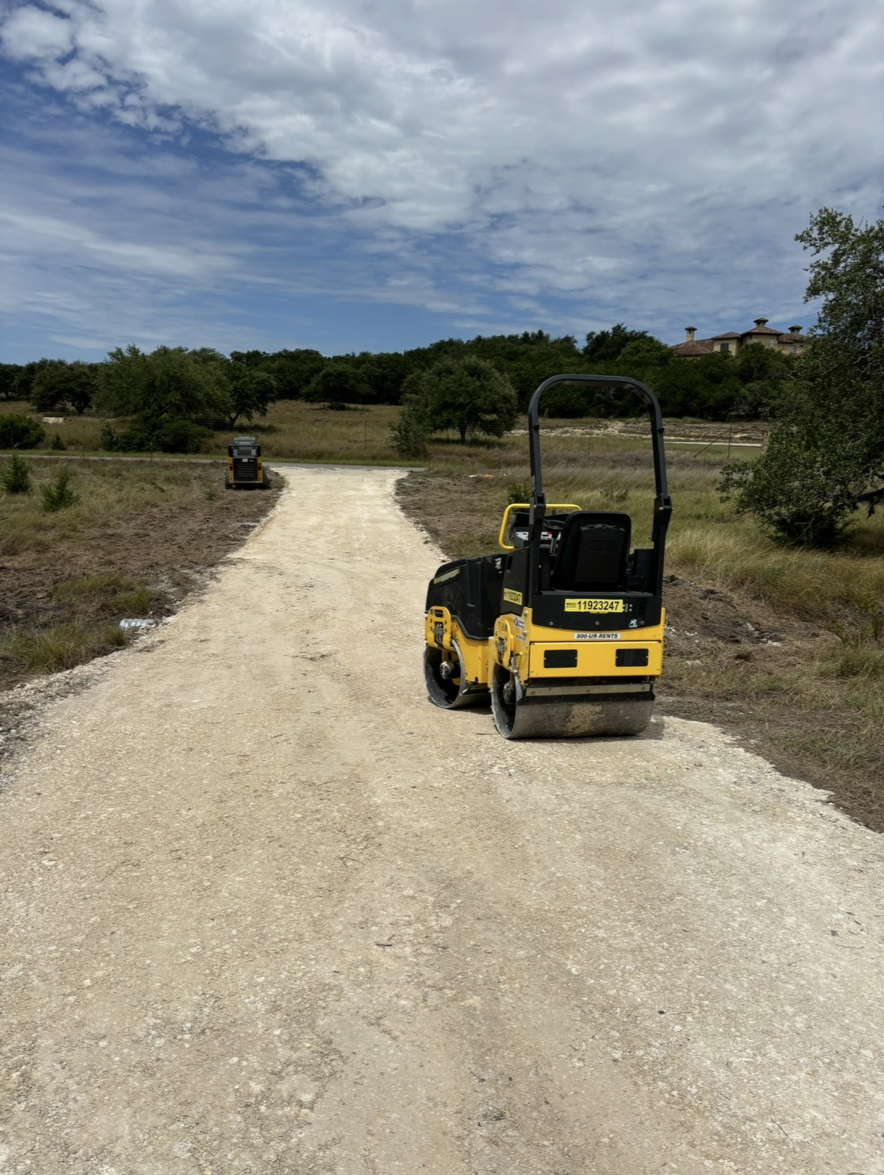 Construction site with road grader leveling dirt road under blue sky.
