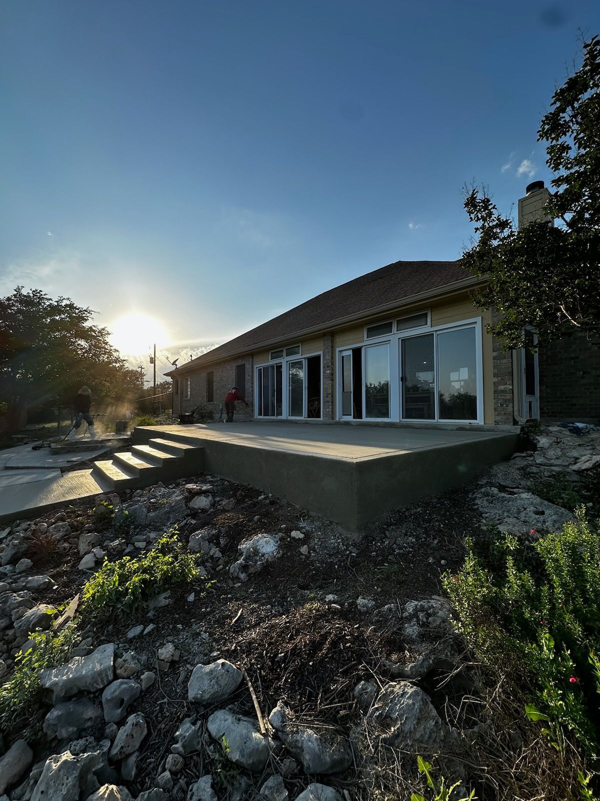 Modern single-story house with large windows on a rocky hillside at sunset