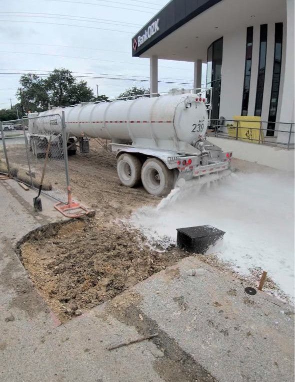 Cement tanker truck pouring concrete at a storefront sidewalk construction site, with wet white slurry on the ground
