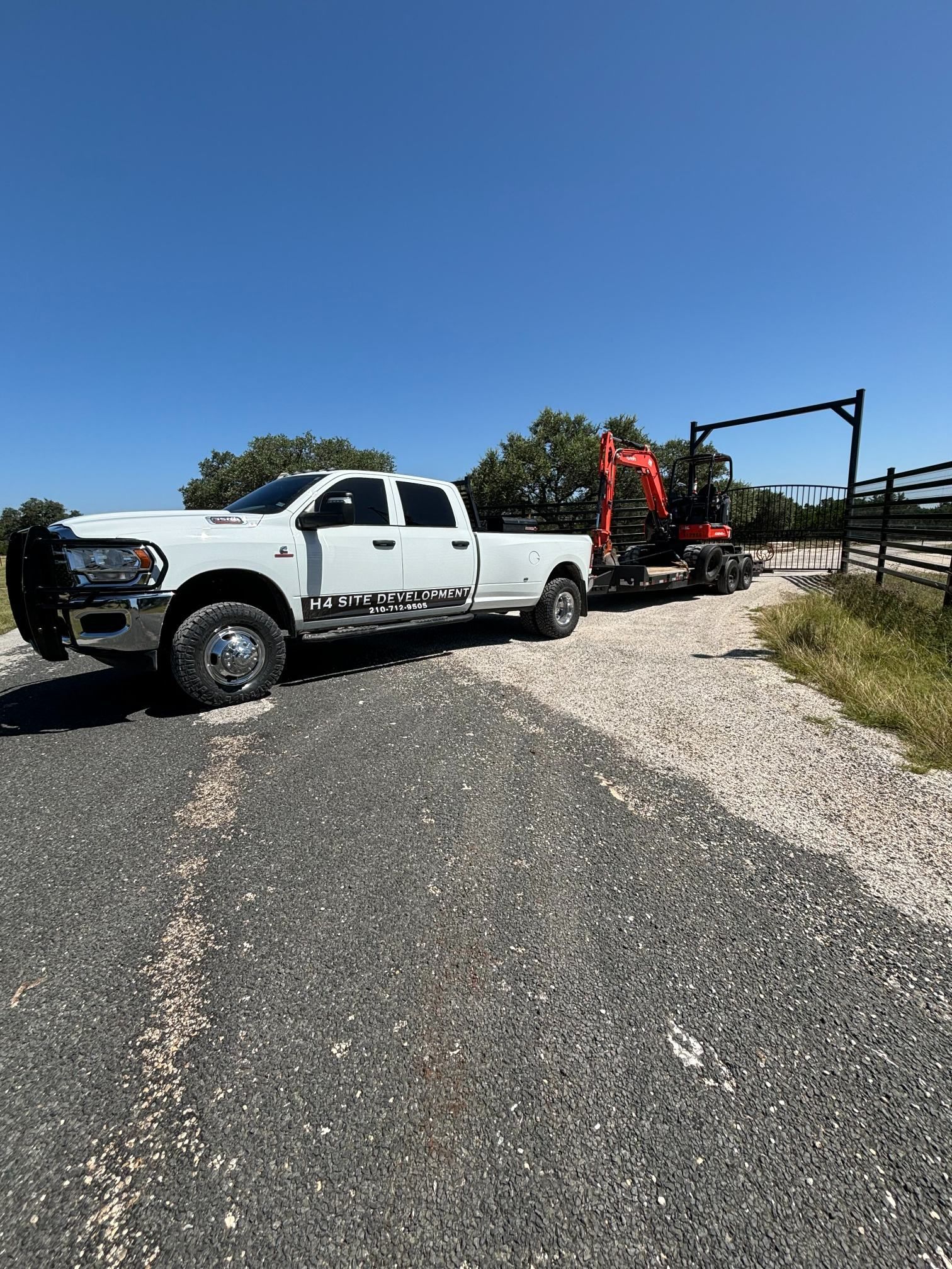 White pickup truck hauling an orange tractor on a gravel road under a clear blue sky
