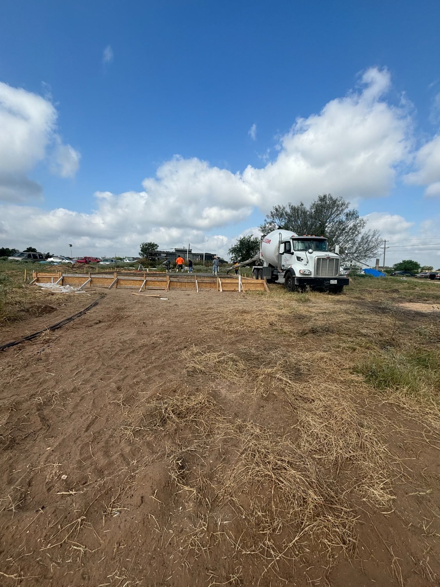 Construction site with a white truck on a dirt lot under a blue, cloudy sky