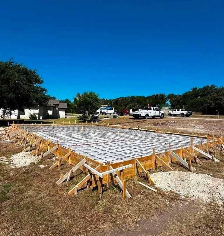Fresh concrete slab foundation with wooden forms and braces on a construction site under a blue sky