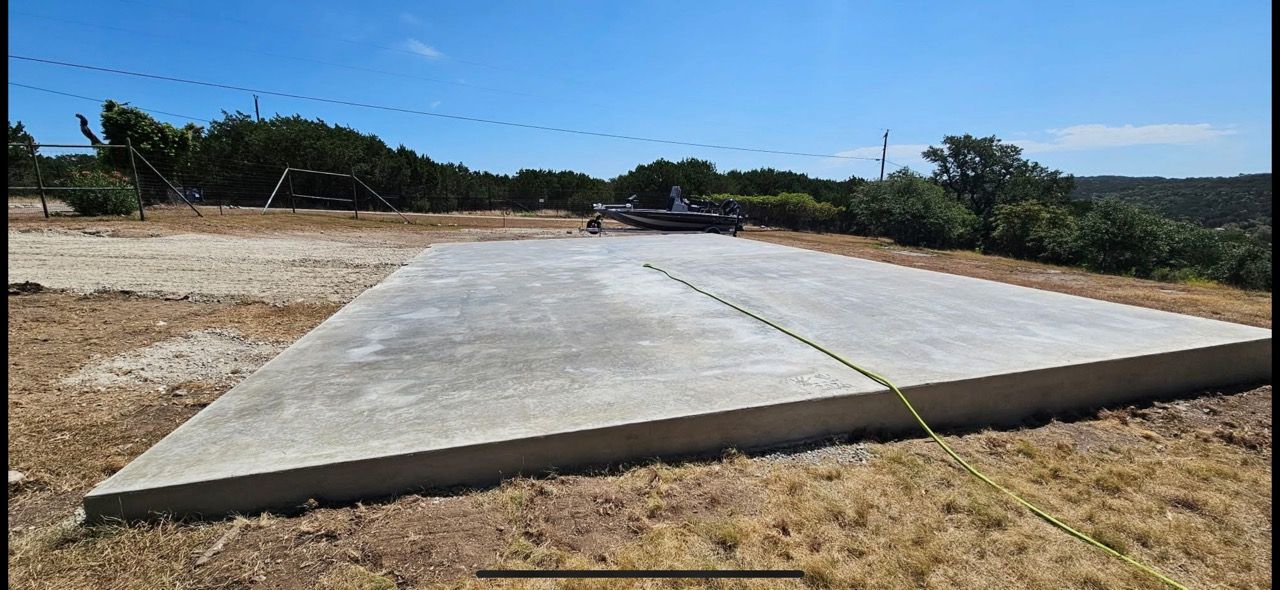 Concrete ramp under construction on a dry, open lot with trees and blue sky in the background