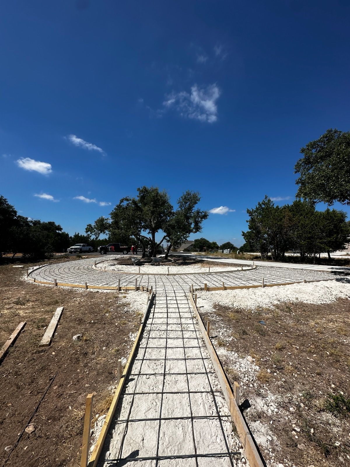 Concrete walkway through a dry, sandy park with scattered trees under a bright blue sky.