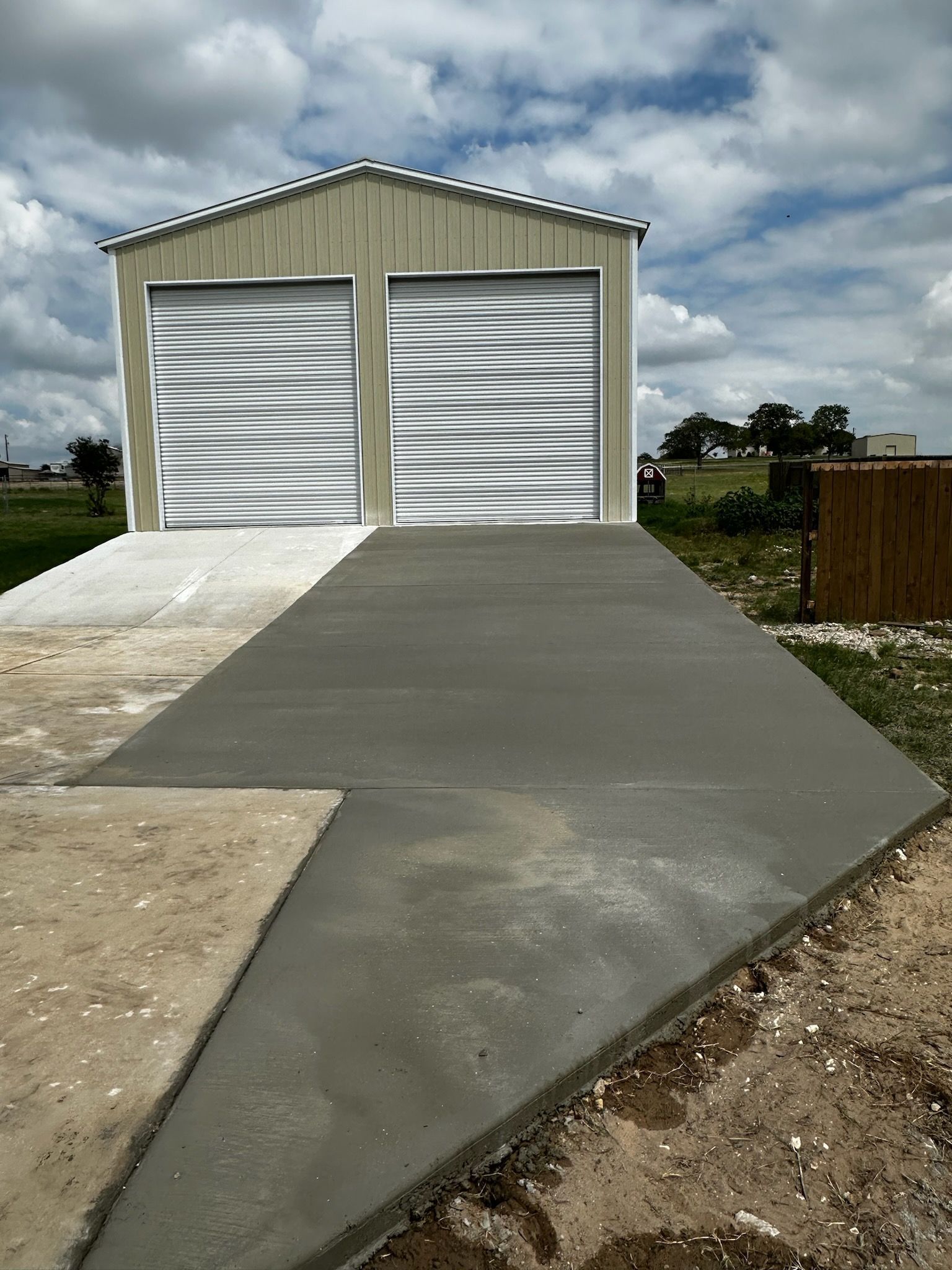 Small metal garage with two silver doors and a fresh concrete driveway under a cloudy sky.