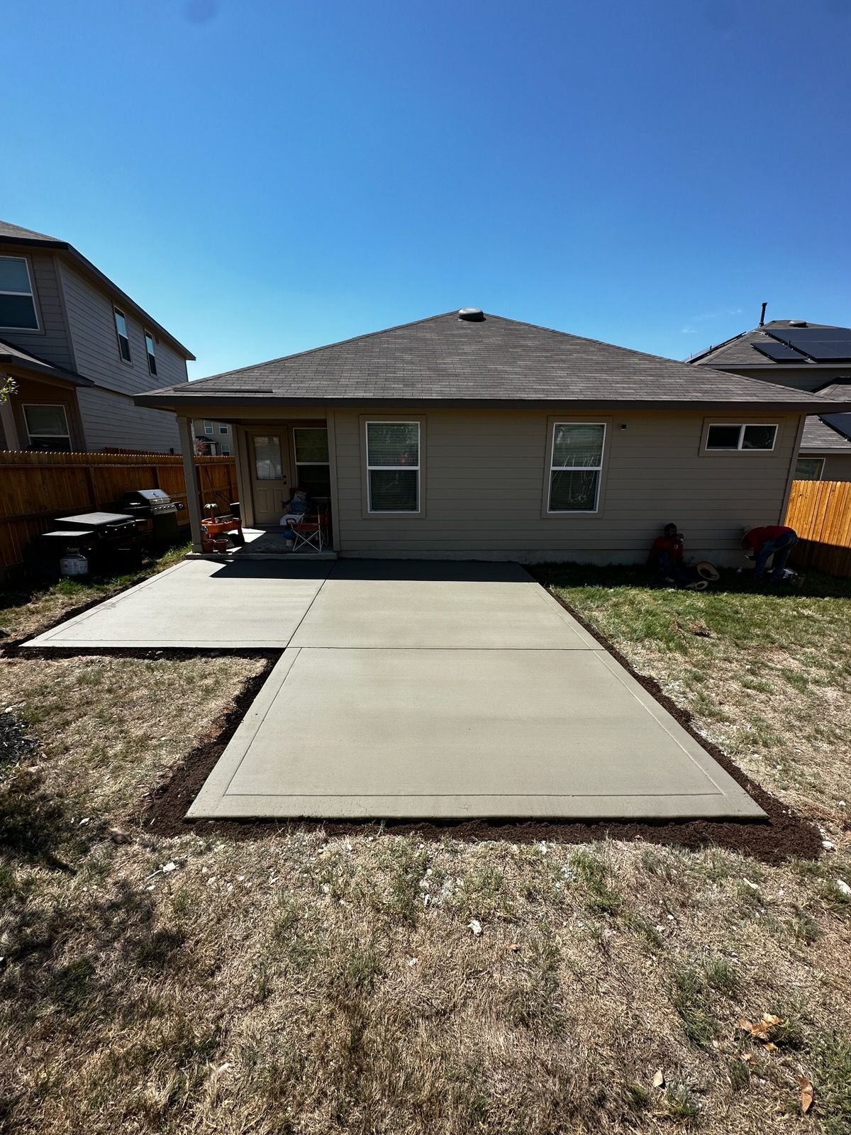 Concrete patio in a backyard with a tan house and clear blue sky.