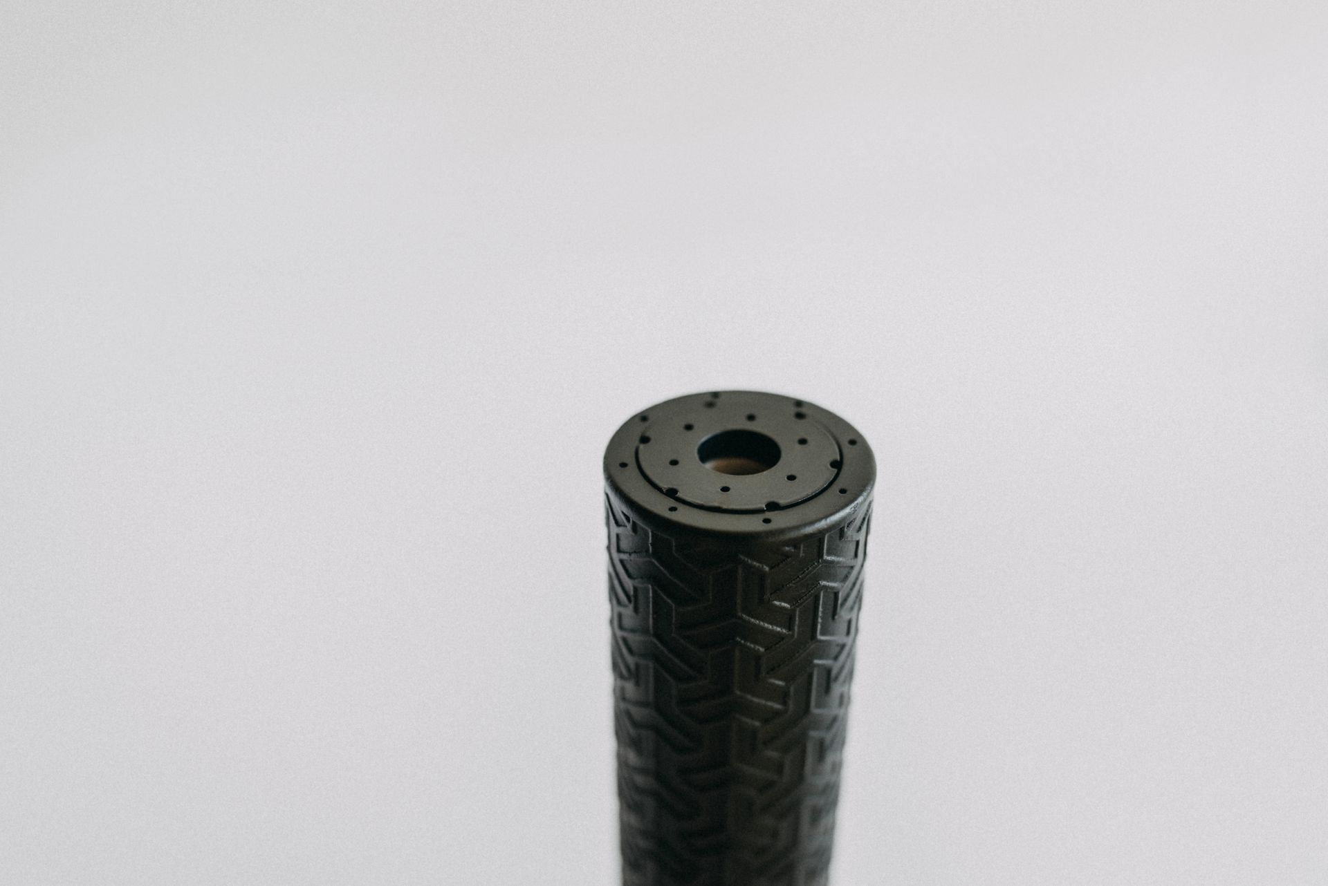 A black cylinder with a hole in the middle is sitting on a white surface.