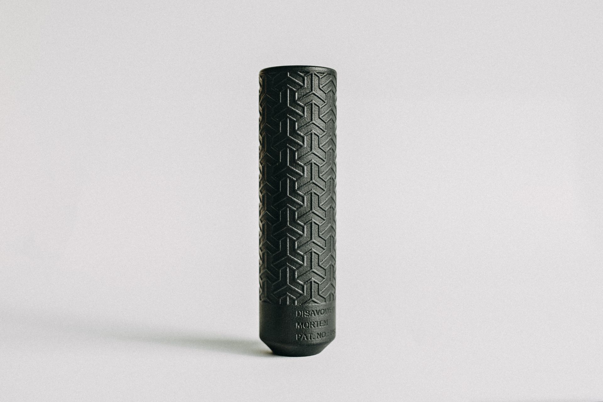 A black cylinder with a pattern on it is sitting on a white surface.