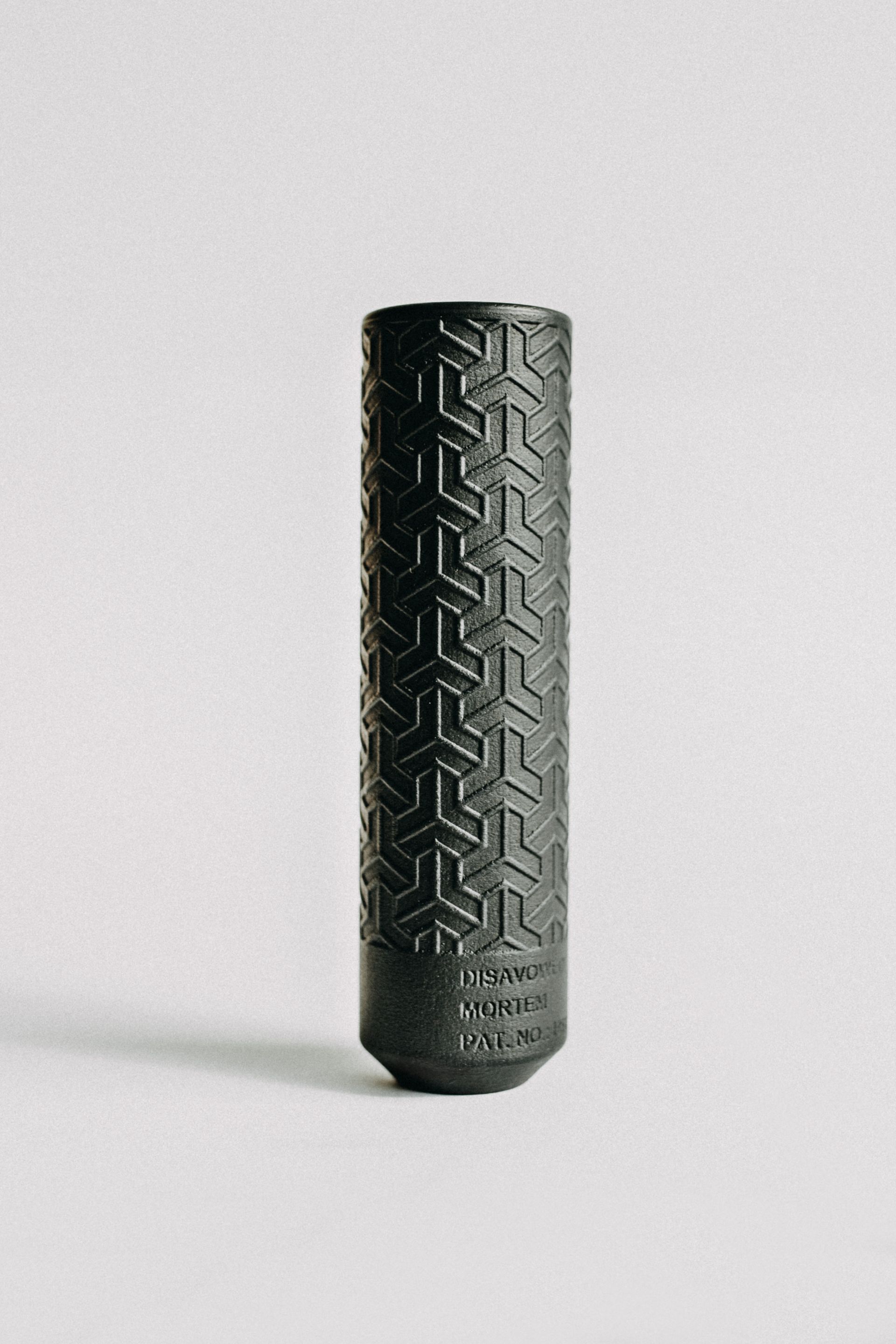 A black vase with a tire pattern on it is sitting on a white surface.