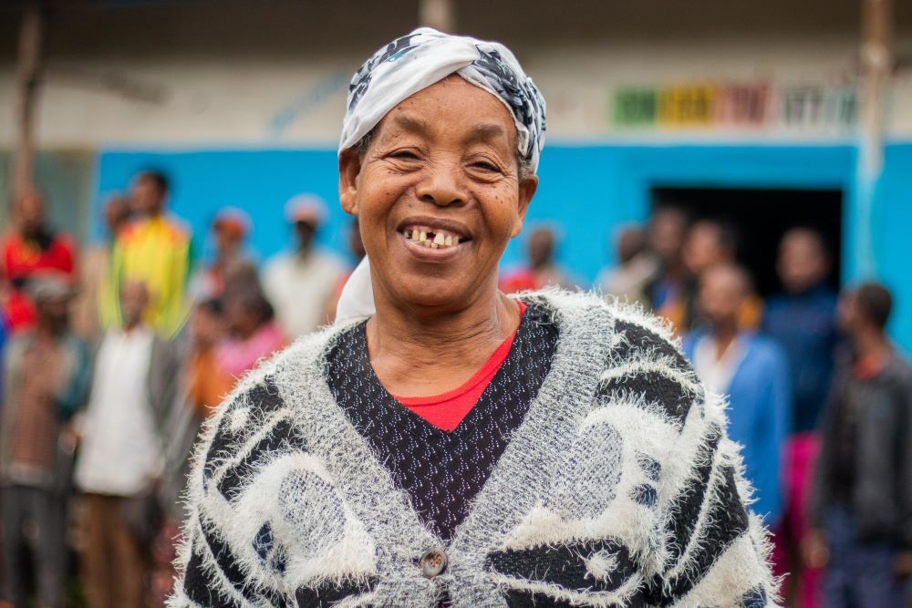 Woman in patterned sweater smiles broadly, standing outside a blue building.