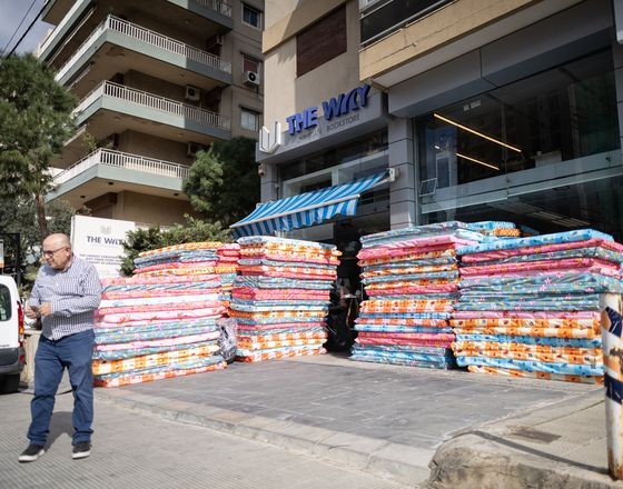 Stacks of colorful bags piled outside a storefront, with a man standing on the sidewalk nearby.