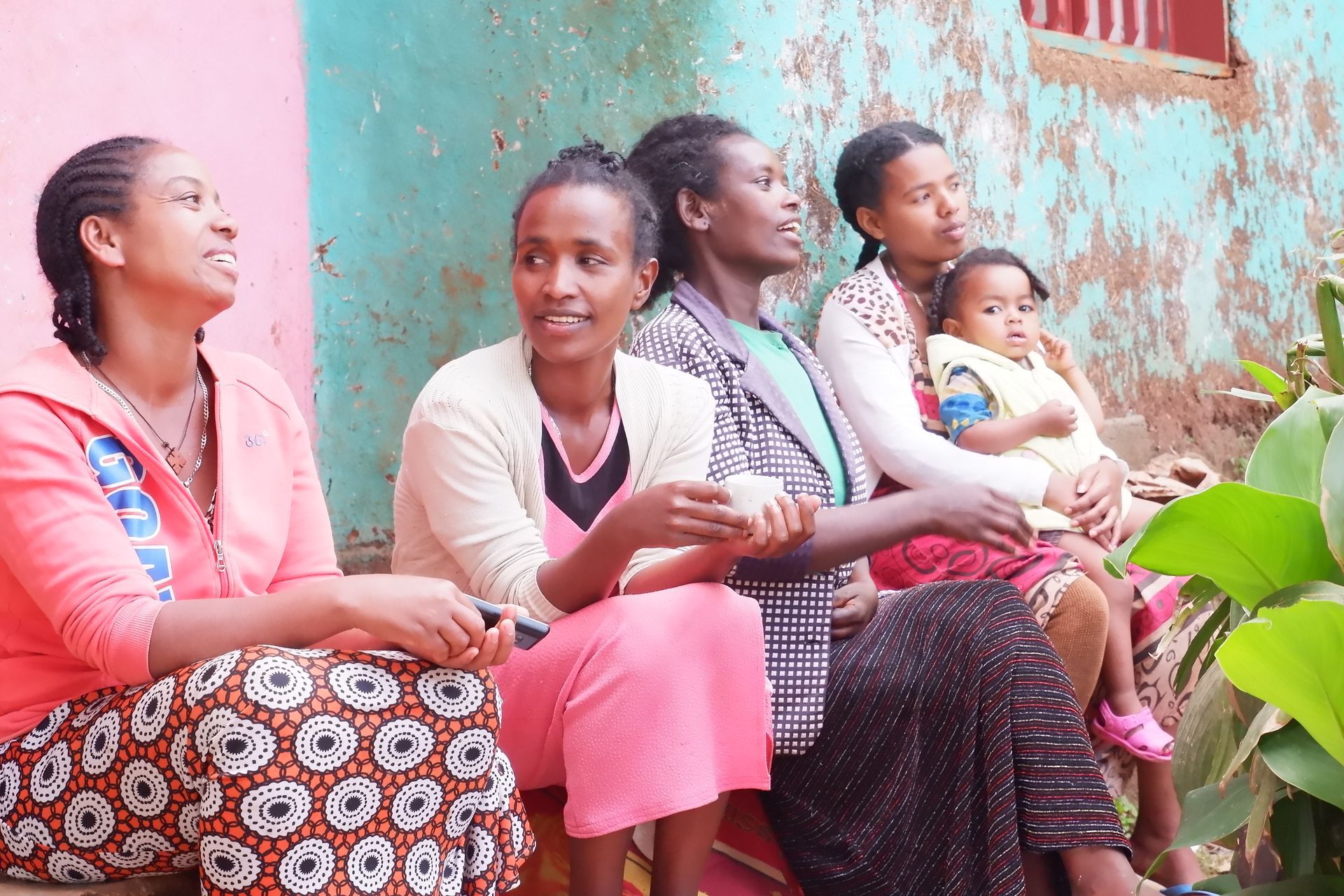 Women and child sitting outside a building, conversing.