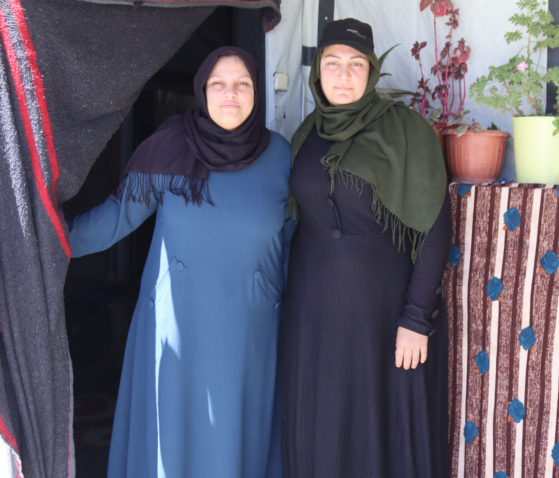 A husband and wife stand in front of a home at a refugee camp