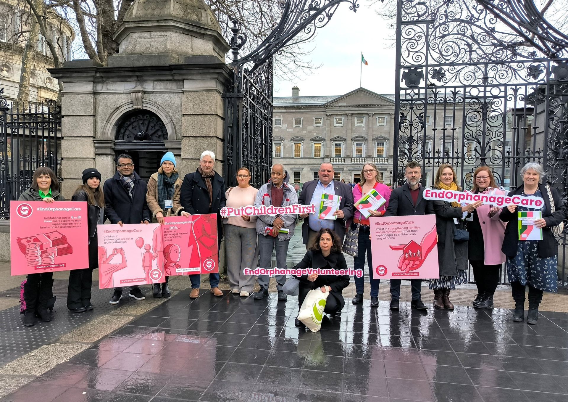 Protesters hold pink signs outside a gated stone building on a rainy day