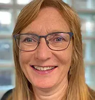Woman with glasses smiles; blonde hair.