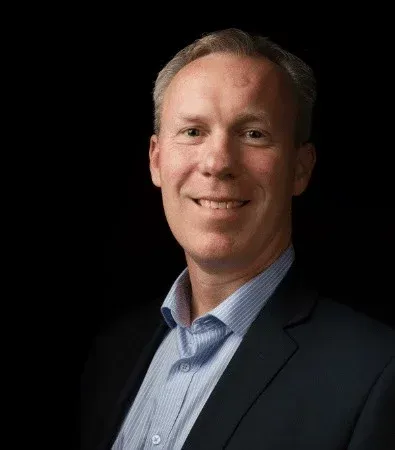 Man in a suit smiles against a black background.