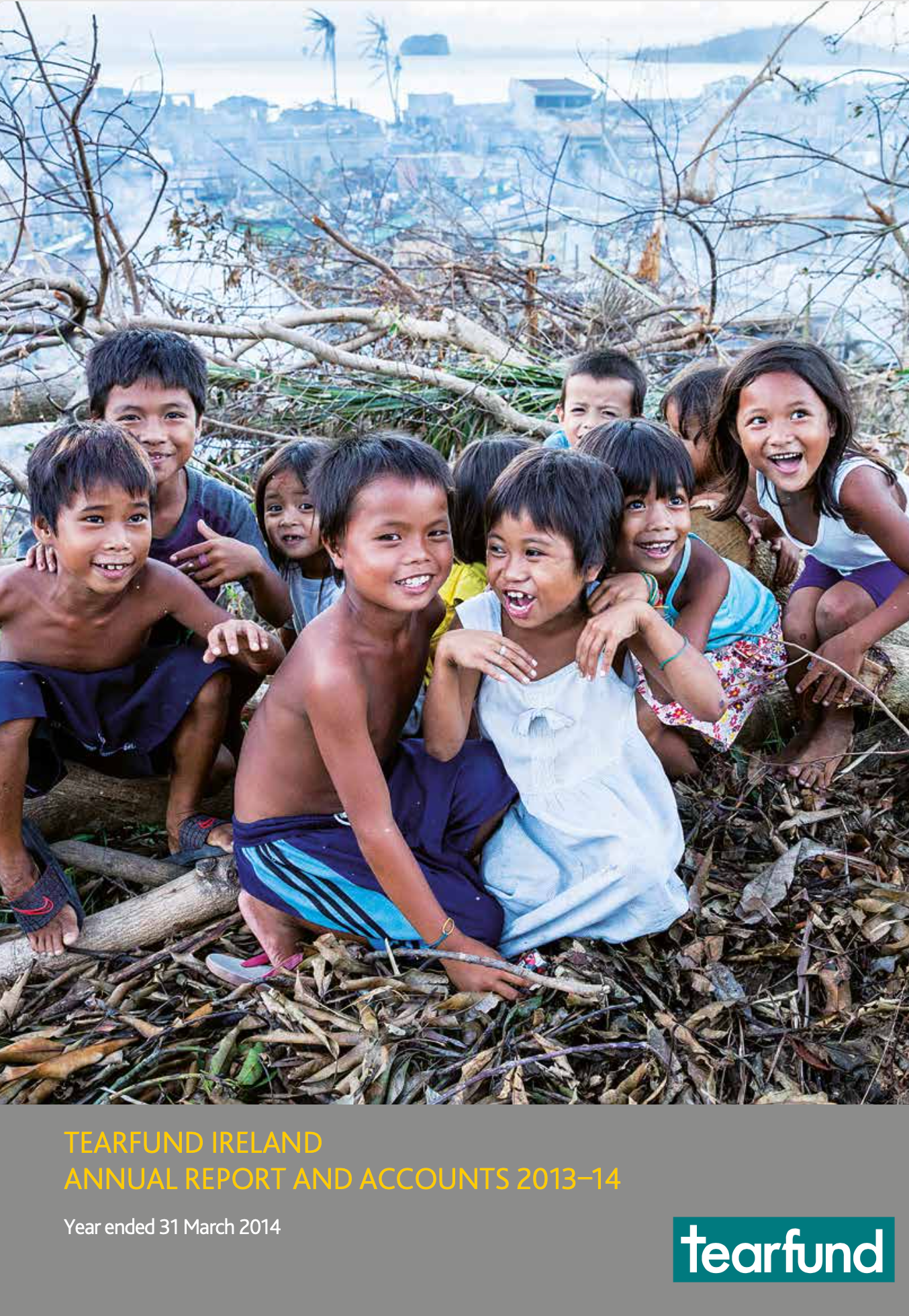 Children smiling in debris, likely after a disaster; background shows damaged buildings.