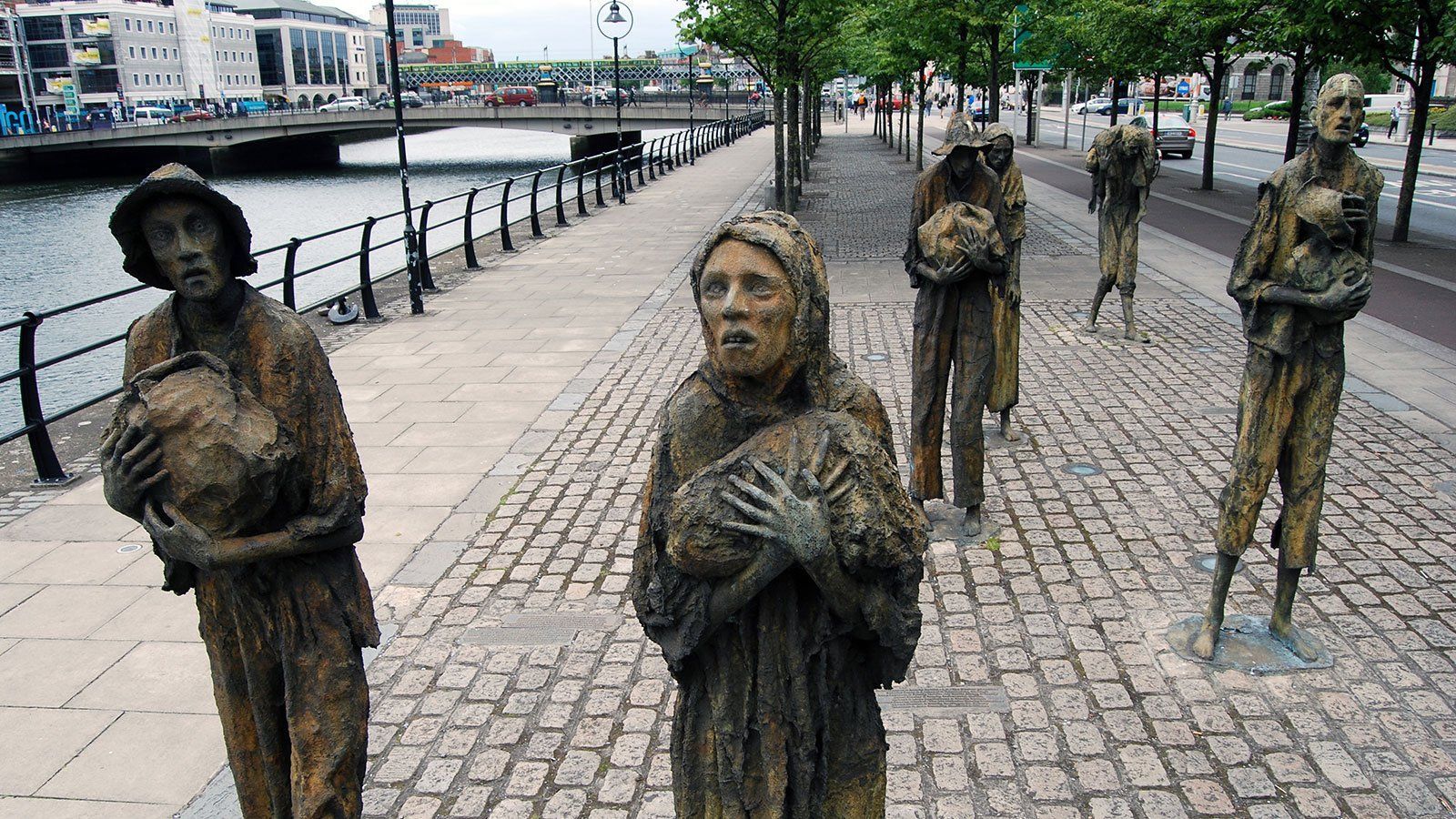 Bronze statues of famine victims lining a brick path along a river.